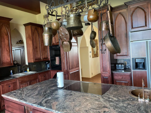 A spacious kitchen with wooden cabinets, a marble countertop, and hanging copper pots and pans.