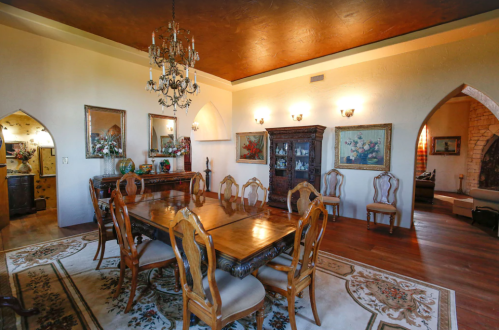 Elegant dining room with a wooden table, ornate chairs, chandelier, and decorative artwork on the walls.