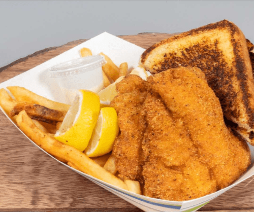 A plate of fried fish with lemon wedges, golden fries, and toasted bread on a wooden surface.