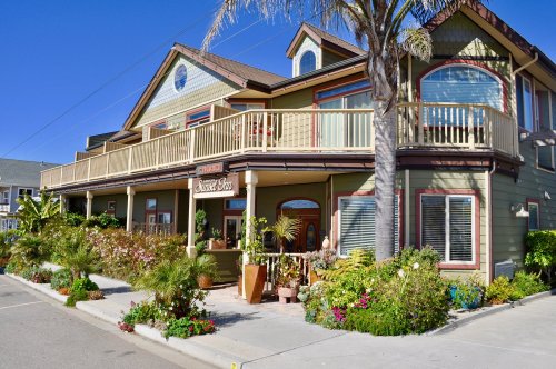 A charming green building with a balcony, surrounded by colorful flowers and palm trees, under a clear blue sky.