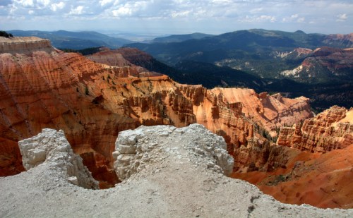 A panoramic view of colorful rock formations and layered cliffs in a vast canyon landscape under a cloudy sky.