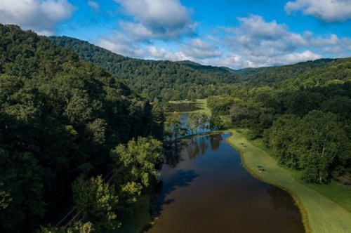 Aerial view of a serene river winding through lush green hills and trees under a partly cloudy sky.
