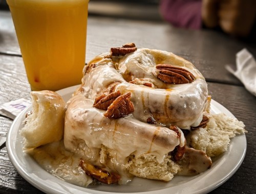 A plate of sticky cinnamon rolls topped with pecans, alongside a glass of orange juice.