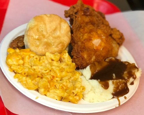 A plate of fried chicken, biscuit, macaroni and cheese, mashed potatoes with gravy, and a side of green beans.