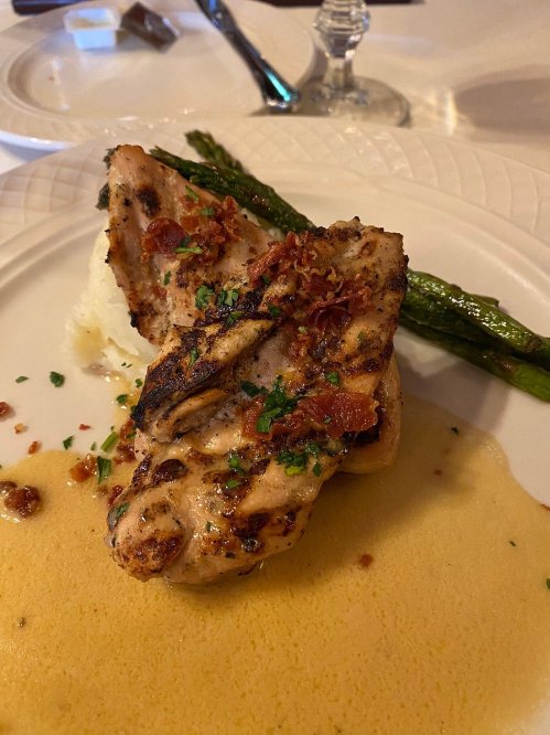 Grilled chicken topped with bacon bits, served with mashed potatoes, asparagus, and a creamy sauce.