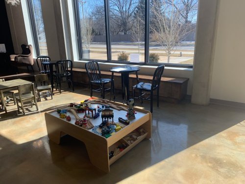 A bright room with large windows, featuring a play table with toys and seating areas.