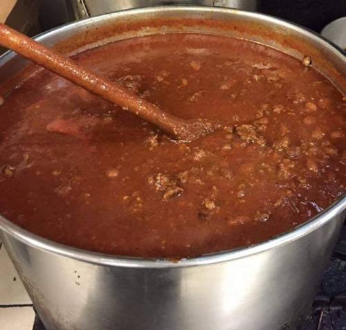A large pot of thick, simmering chili with a wooden spoon resting inside.