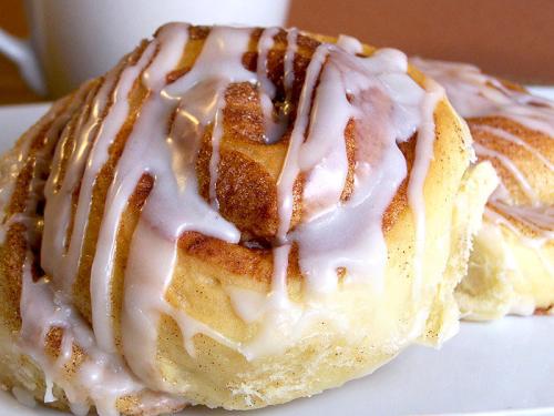 Two freshly baked cinnamon rolls drizzled with white icing, served on a plate.