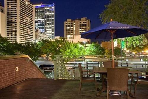 A nighttime cityscape featuring tall buildings, a patio with a table and chairs, and an umbrella.