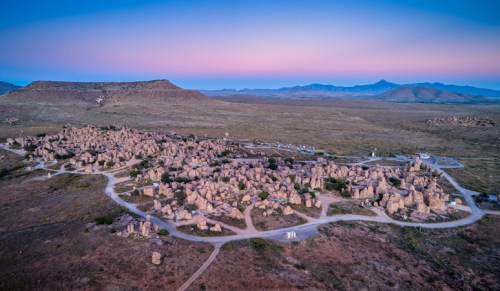 Aerial view of a rocky landscape with unique formations and distant mountains under a pastel sky at dusk.