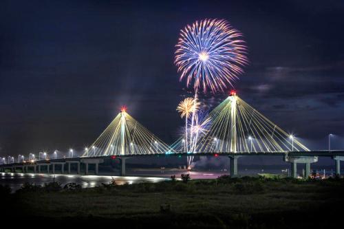 A bridge illuminated at night with colorful fireworks exploding in the sky above it.