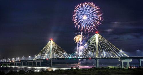 A bridge illuminated at night with colorful fireworks bursting in the sky above it.