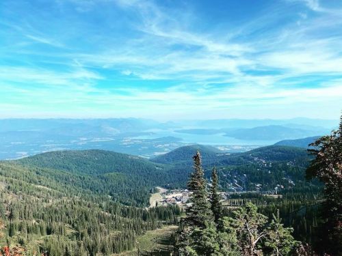 A panoramic view of lush green mountains and a serene lake under a blue sky with wispy clouds.