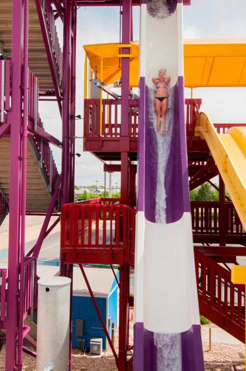 A person slides down a colorful water slide at a water park, surrounded by vibrant structures and a clear sky.