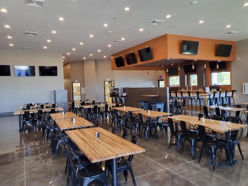 A spacious restaurant interior with wooden tables, black chairs, and multiple TVs on the walls. Brightly lit and modern.