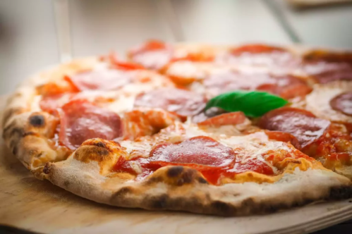 A close-up of a pepperoni pizza with melted cheese and a fresh basil leaf on top, resting on a wooden surface.