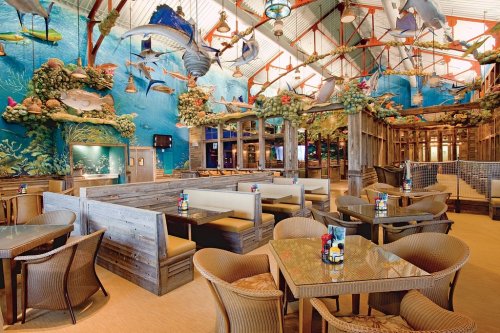 A vibrant restaurant interior with ocean-themed decor, wooden booths, and tropical fish murals on the walls.