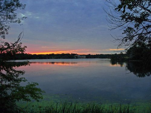 A serene lake at sunset, reflecting colorful skies and surrounded by trees.