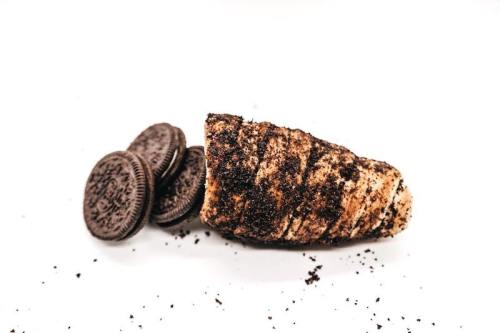 A chocolate-filled pastry cone topped with crushed Oreos, next to whole Oreo cookies on a white background.