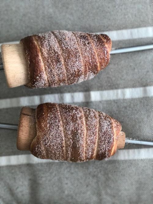 Two freshly baked, spiral-shaped pastries coated in sugar, resting on wooden skewers against a striped background.