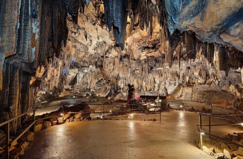 A vast cave interior with dramatic stalactites and stalagmites, illuminated by soft lights along a stone pathway.
