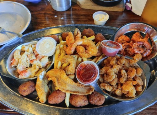 A metal platter filled with fried seafood, including shrimp, fish, and crab, accompanied by sauces and fries.