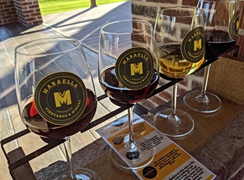 Four wine glasses with red, white, and rosé wines, displayed on a wooden rack at a vineyard.