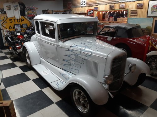 A vintage white car with blue flame designs, displayed in a retro-themed garage with checkered flooring.