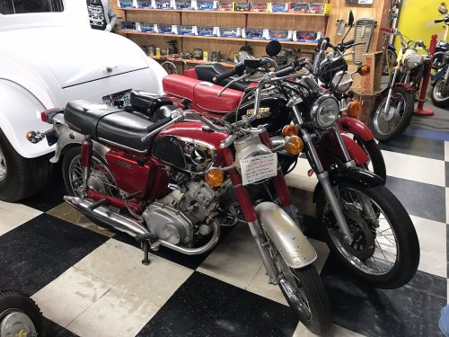 Two vintage motorcycles in a garage, one red and silver, the other red and black, alongside a classic white car.