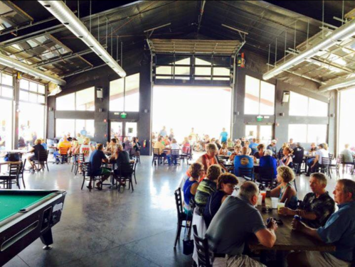 A bustling indoor dining area with people seated at tables, large windows, and a pool table in the foreground.