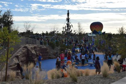 A vibrant playground filled with children playing, climbing structures, and enjoying outdoor activities under a blue sky.