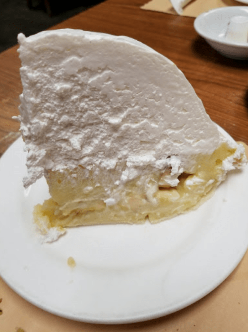 A slice of banana cream pie with a thick layer of whipped cream on top, served on a white plate.