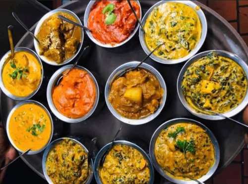 A platter of various colorful Indian dishes in small bowls, featuring curries and vegetables, garnished with herbs.