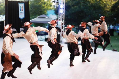 A group of dancers in traditional attire performing a lively dance on stage outdoors.