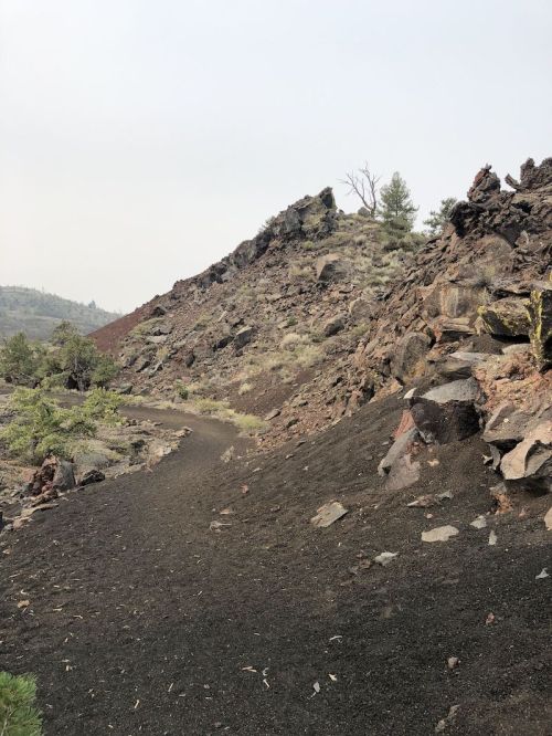 A winding path through rocky terrain with sparse vegetation and a hazy sky in the background.