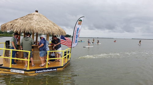 A tiki boat with people on it near paddleboarders on a cloudy day in the water.