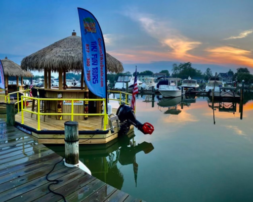 A serene marina at sunrise, featuring a tiki bar, boats, and calm waters reflecting the colorful sky.