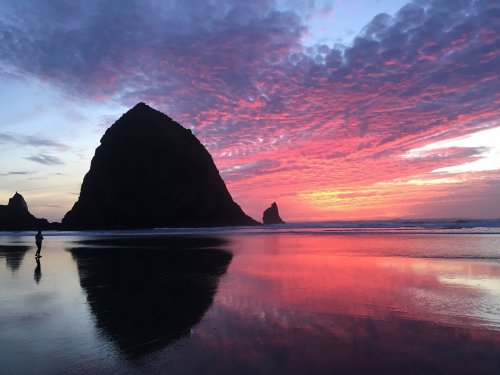 A serene beach at sunset, featuring a silhouette of a large rock formation and vibrant pink and purple clouds.