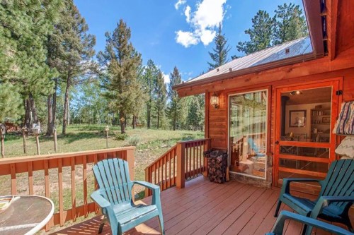 A wooden deck with two chairs overlooks a forested area and blue sky, inviting relaxation in nature.
