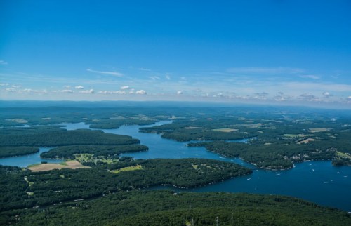 Aerial view of a vast landscape featuring lakes, forests, and rolling hills under a clear blue sky.