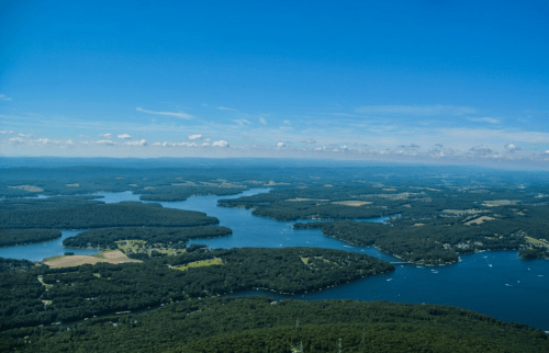 Aerial view of a vast landscape featuring lakes, forests, and rolling hills under a clear blue sky.