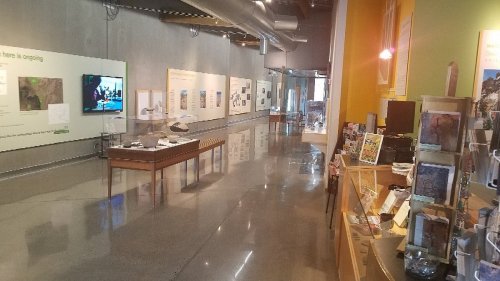 Interior of a museum exhibit featuring displays, a TV screen, and informational panels along the walls.