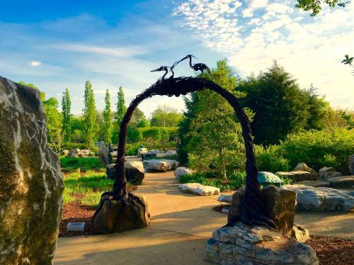 A scenic garden path with a decorative arch featuring two birds, surrounded by lush greenery and rocks.