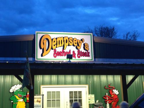 Sign for Dempsey's Seafood & Steak restaurant, featuring colorful graphics and a green building under a twilight sky.