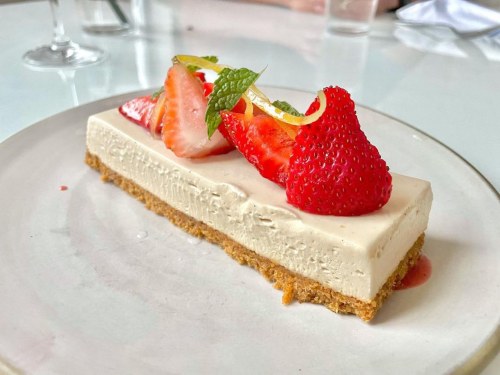 A slice of creamy cheesecake topped with fresh strawberries and mint on a white plate.