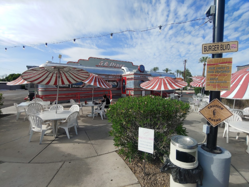 A retro diner with red and white umbrellas, outdoor seating, and a sign for Burger Blvd under a blue sky.