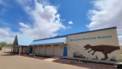 Exterior of the Misalands Dinosaur Museum, featuring a dinosaur mural and a blue roof under a cloudy sky.