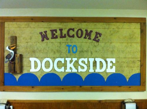 Sign reading "Welcome to Dockside" with decorative waves and a wooden pelican.