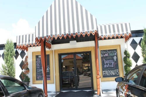 A colorful storefront with a striped awning, featuring a chalkboard sign advertising wine, beer, and fauxnuts.