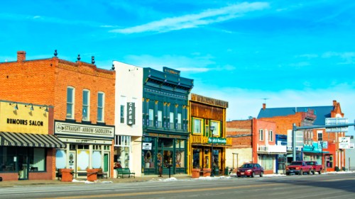 A row of historic buildings with shops and a blue sky in the background, showcasing a small-town atmosphere.